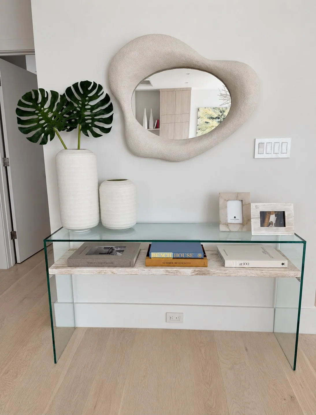 Glass console with vases, books, and sculptural mirror