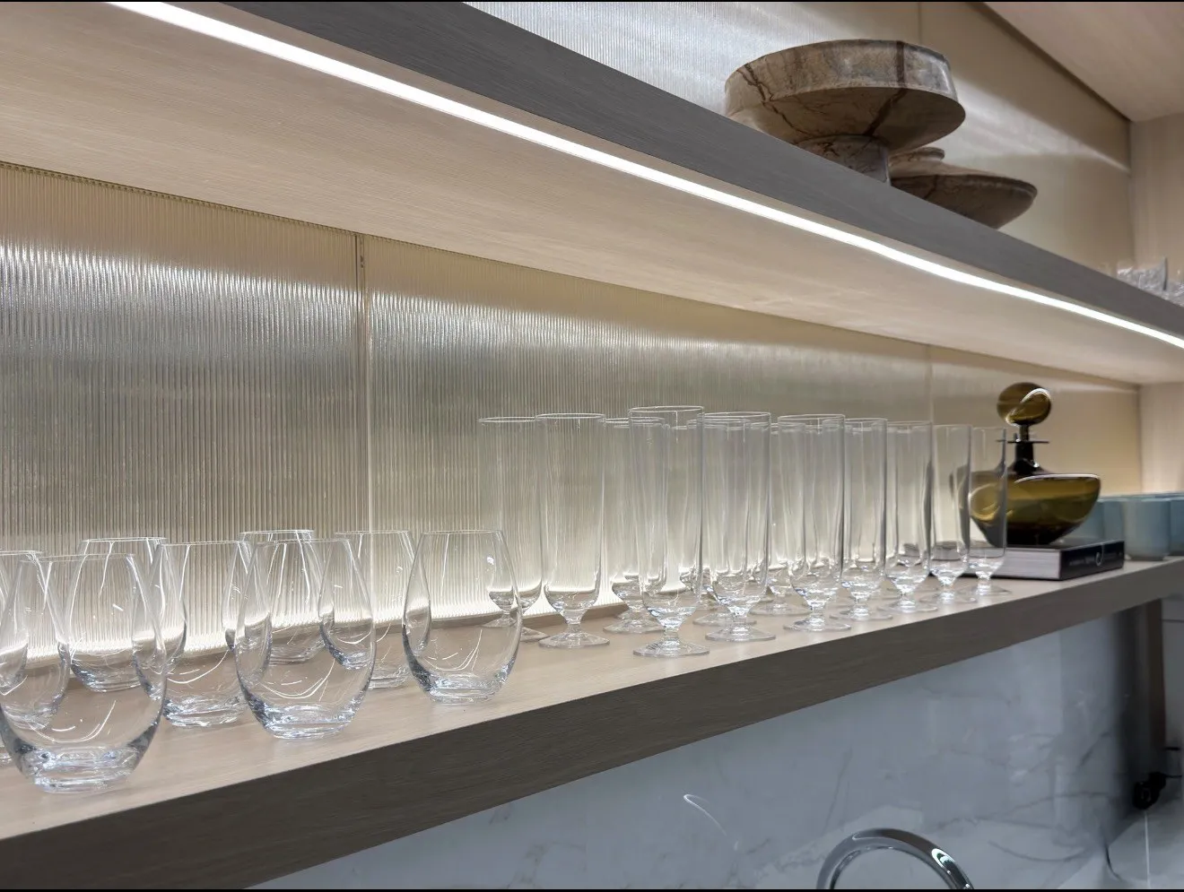 Ribbed glassware and an amber vessel on lit oak shelving in a Manhattan corporate café