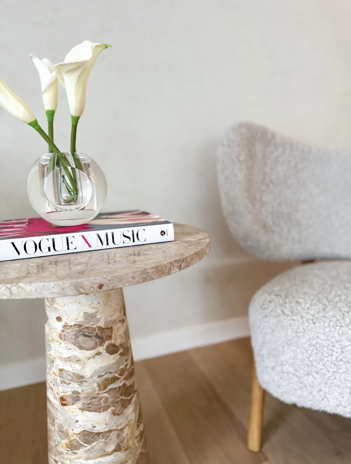 Calla lilies on a stone side table beside an upholstered chair