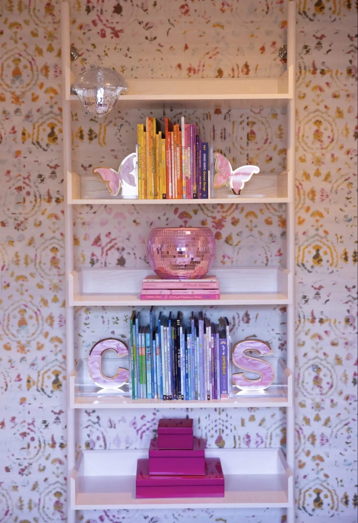 Patterned bookcase styled with colorful books and pink objects
