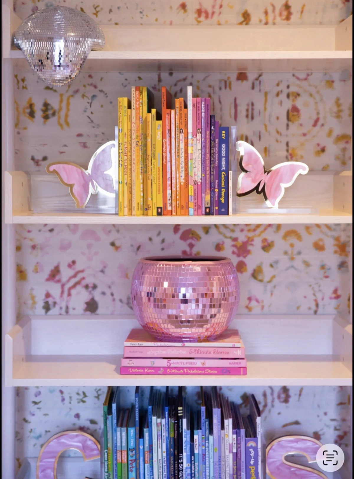 Close-up of colorful books and pink glass on patterned shelves