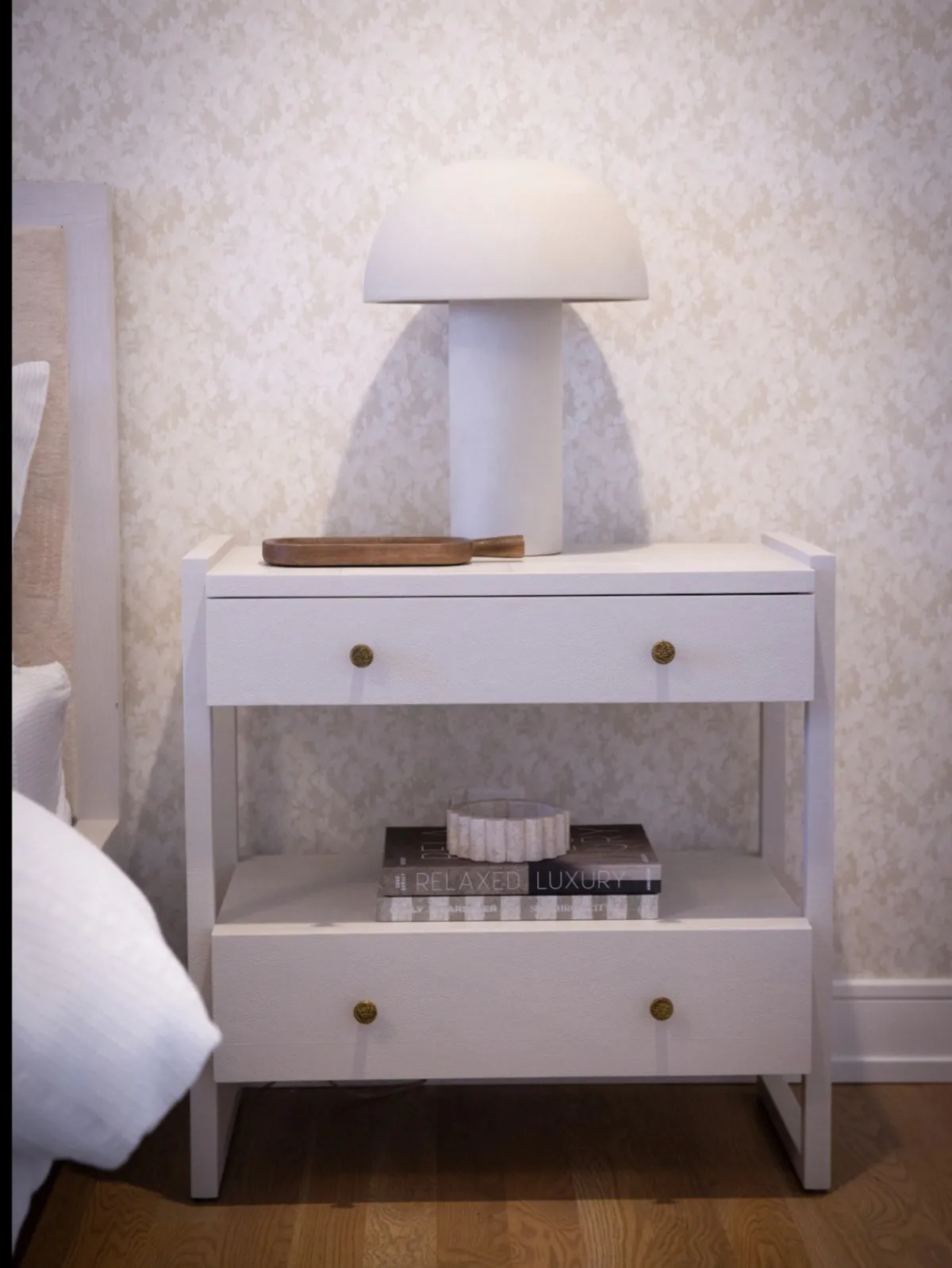 White bedside table styled with a lamp, tray, and books