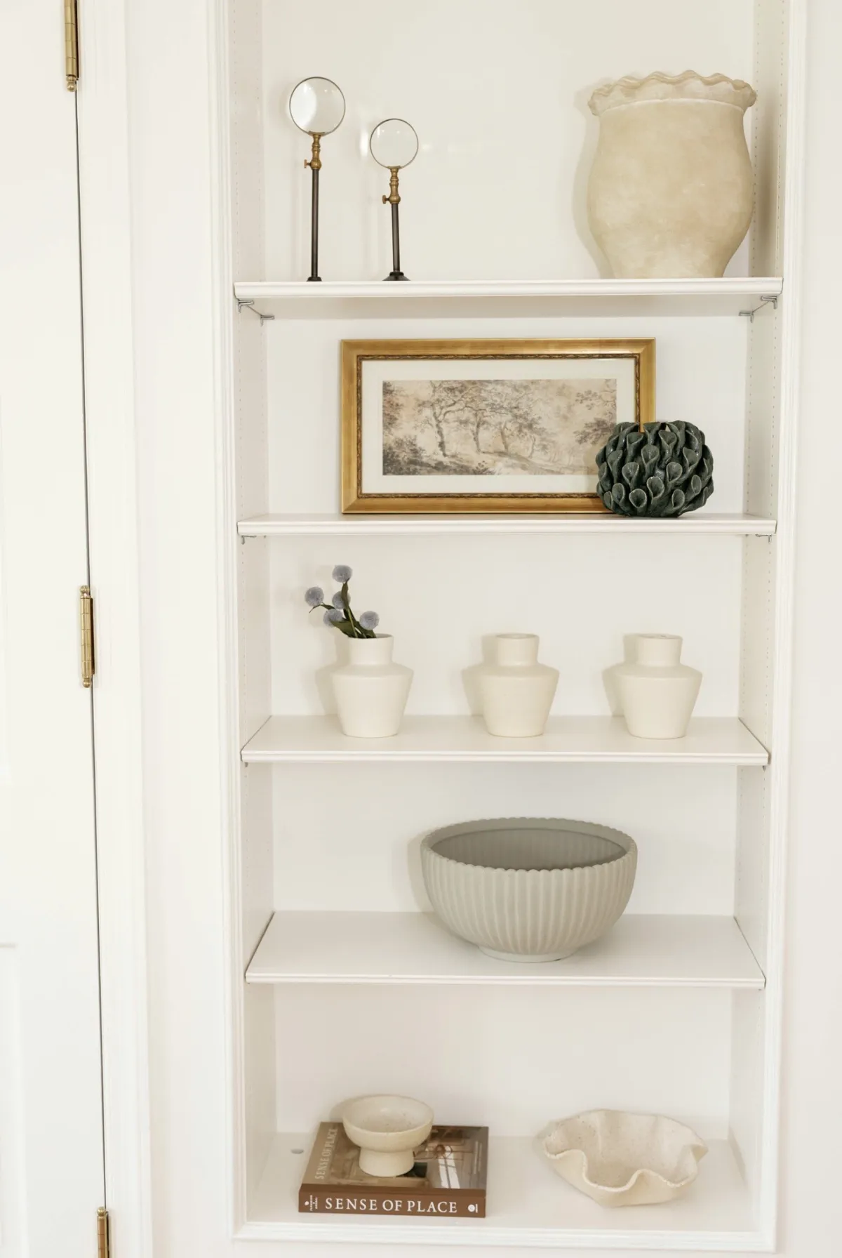 Styled built-in shelves with framed art, ceramic vessels, and a ribbed bowl