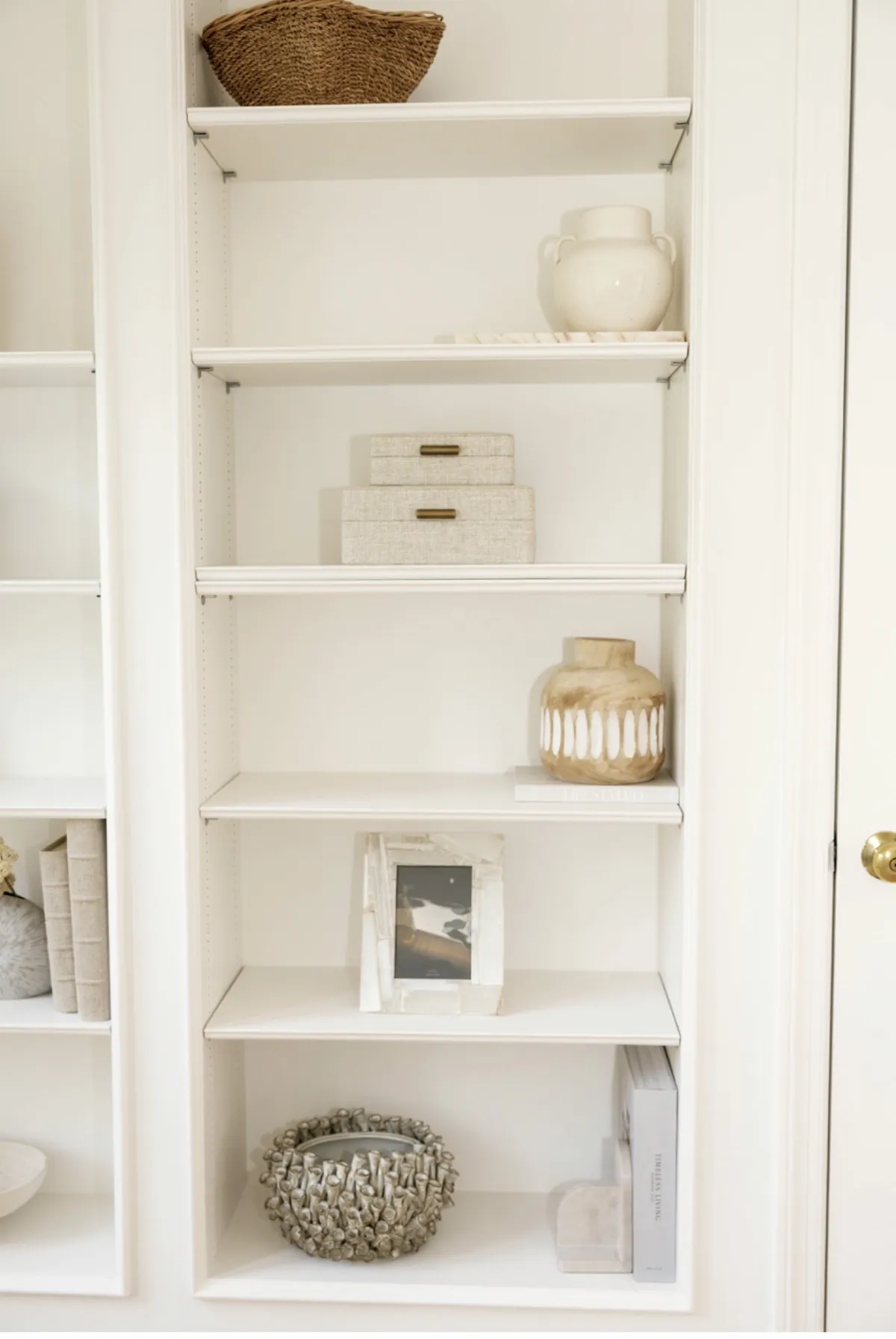 Neutral decorative objects, woven basket, and framed photograph on white shelves