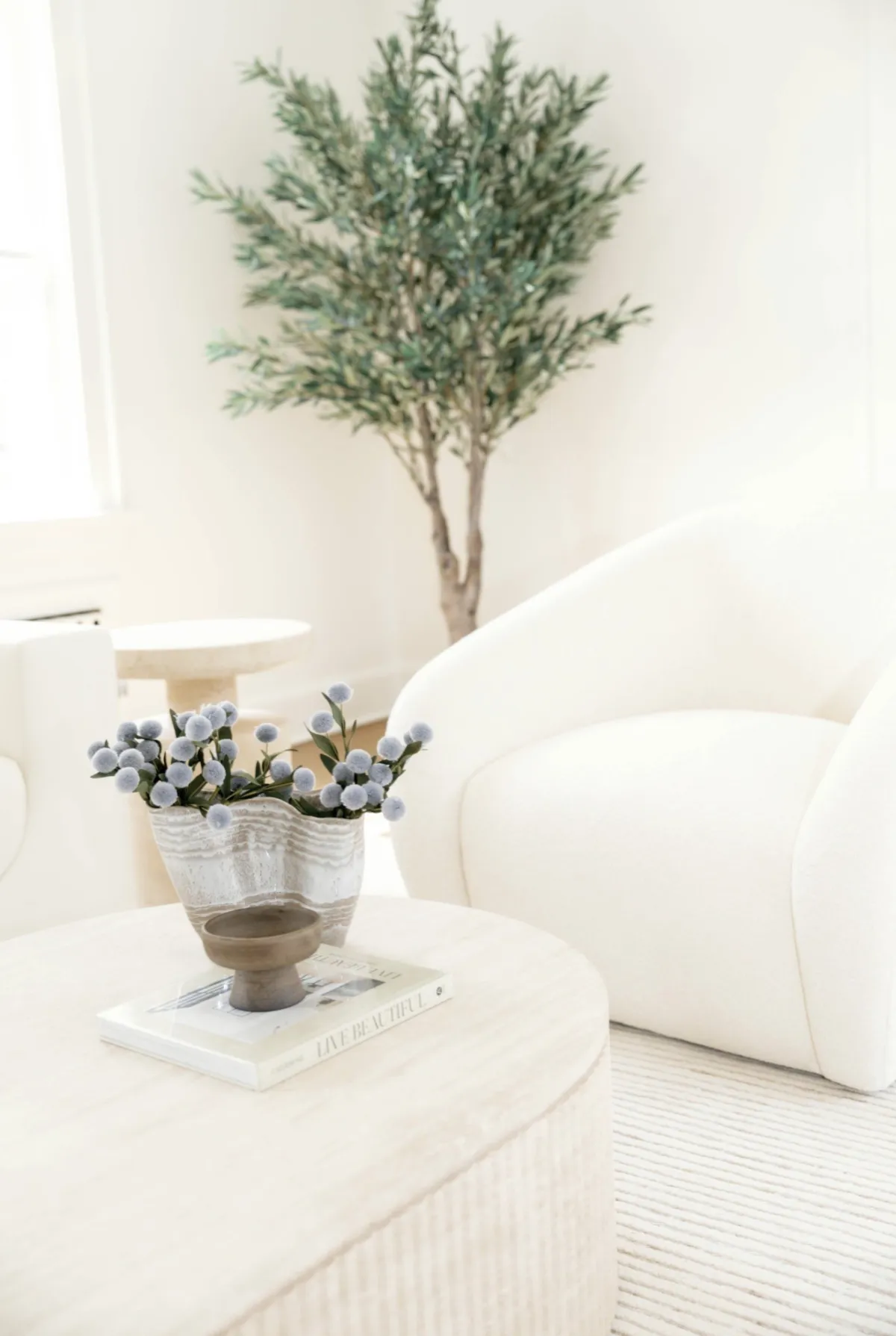 Soft blue flowers and sculptural bowl on a coffee table beside a curved chair