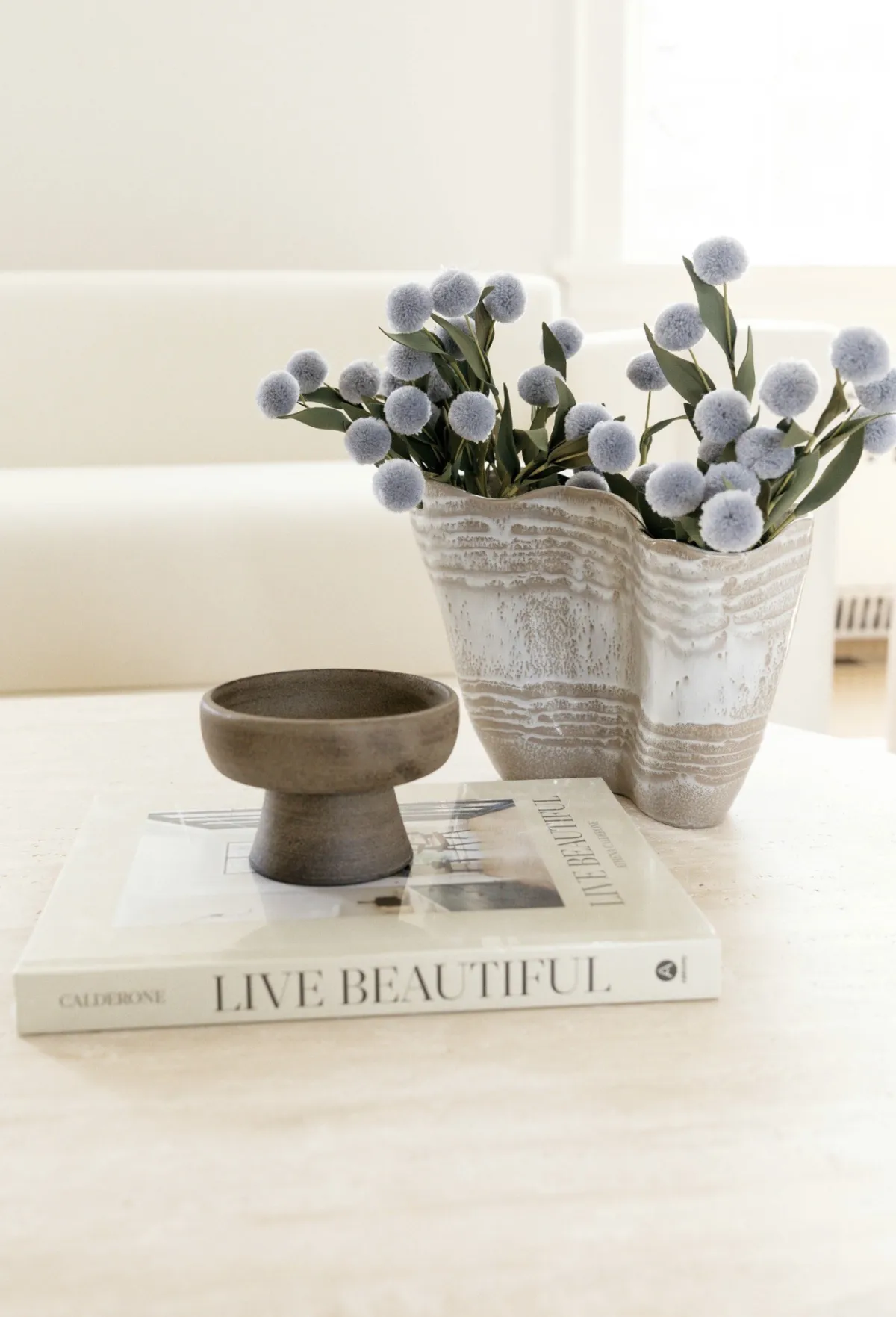 Blue flowers and a small bowl styled over a Live Beautiful book
