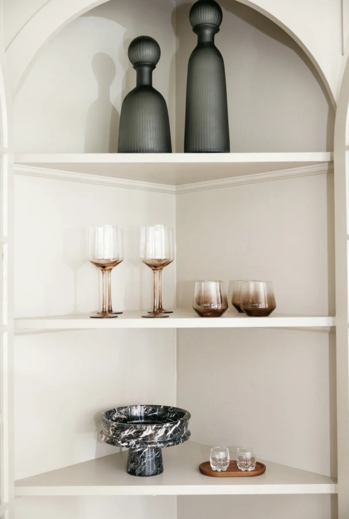 Arched bar shelves with charcoal vessels, rose glassware, and marble bowl