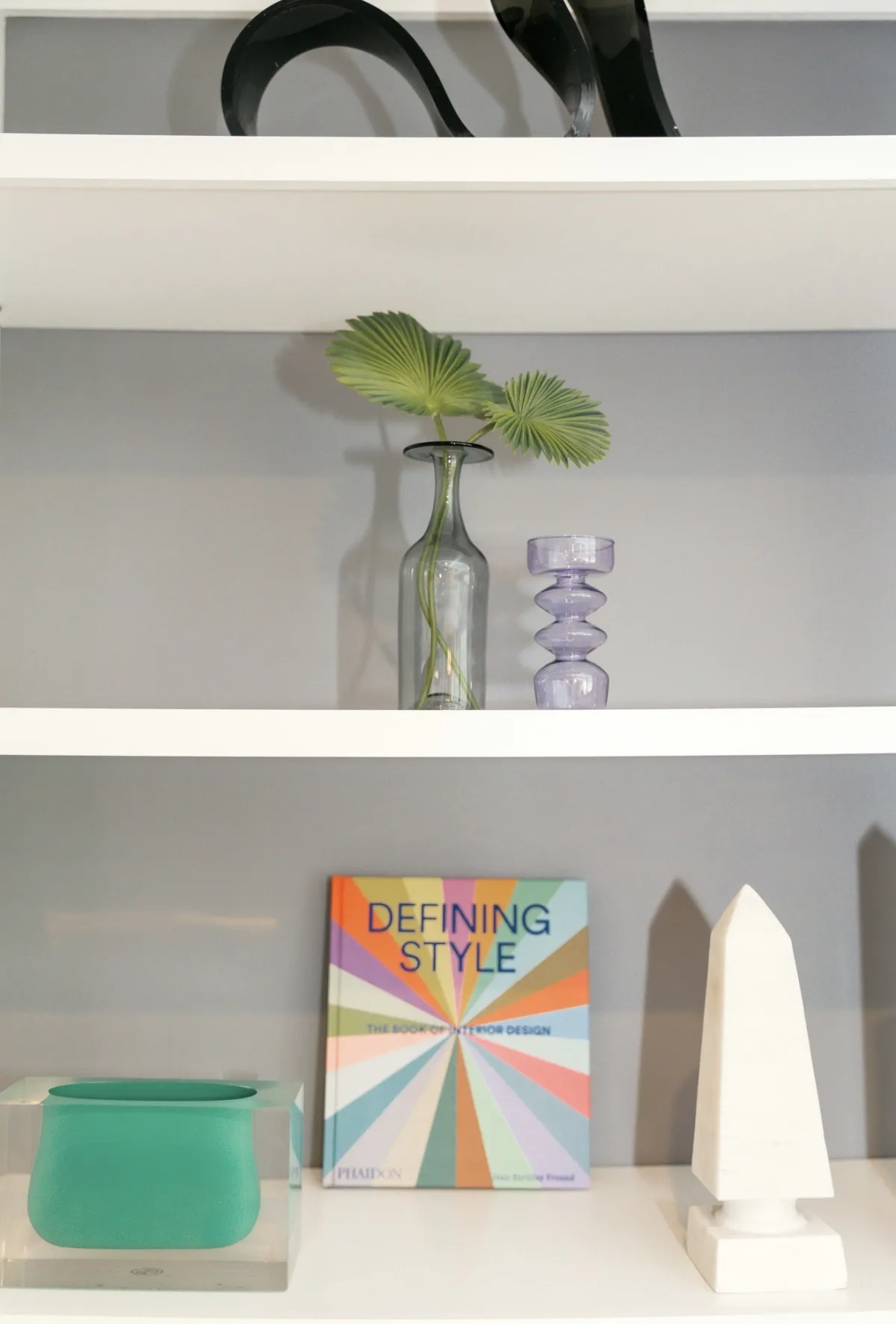 Palm leaf, a Defining Style book and a white obelisk on built-in shelves