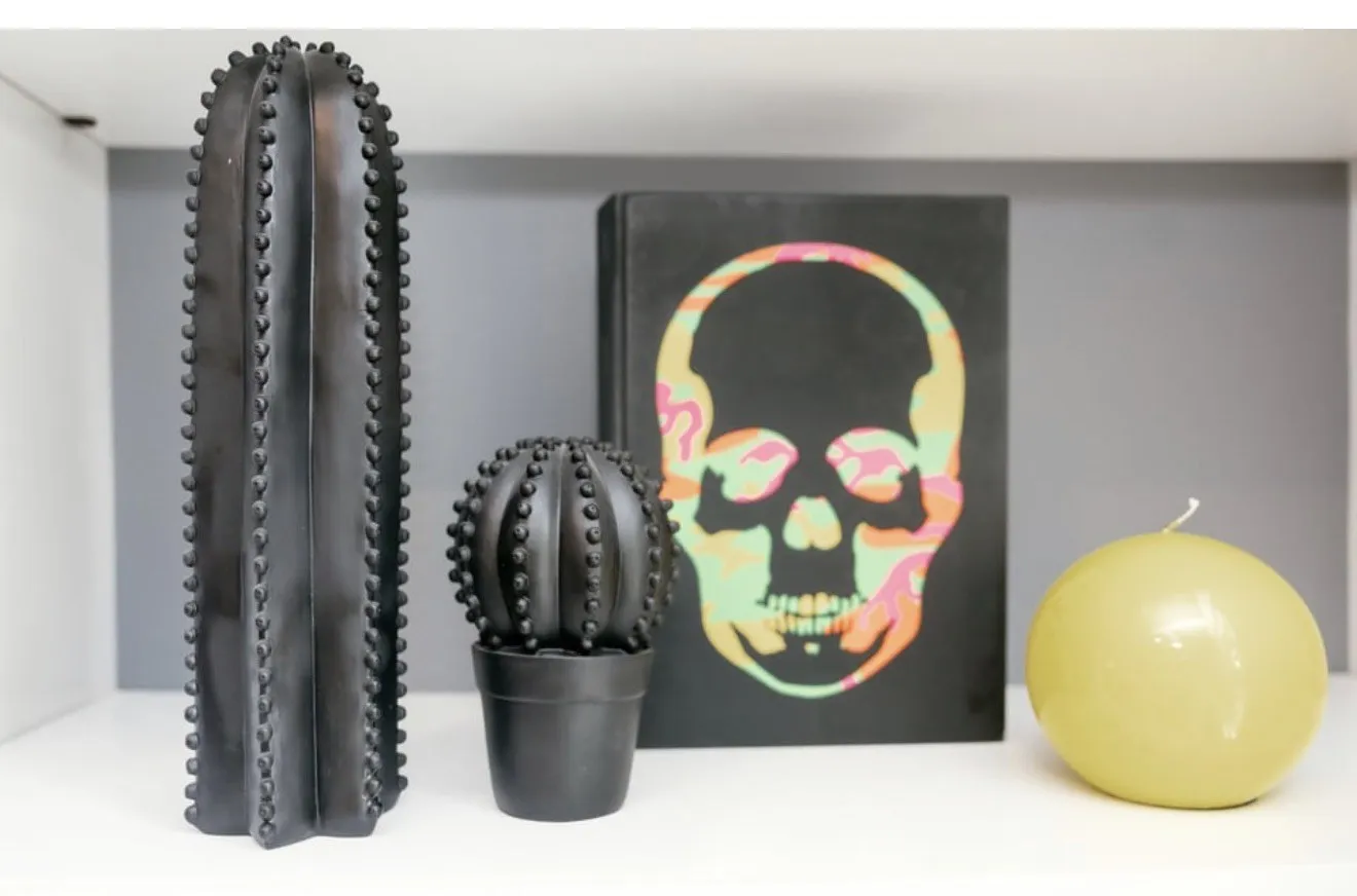 Black cactus sculptures, skull artwork and a yellow candle on a shelf