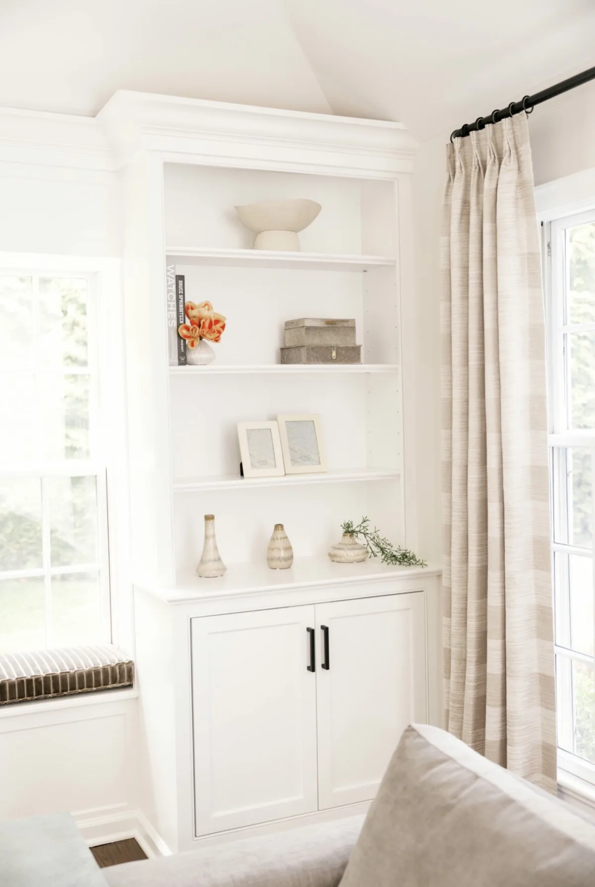 White built-in shelves styled with orange flowers and ceramics beside tall drapery and a window seat