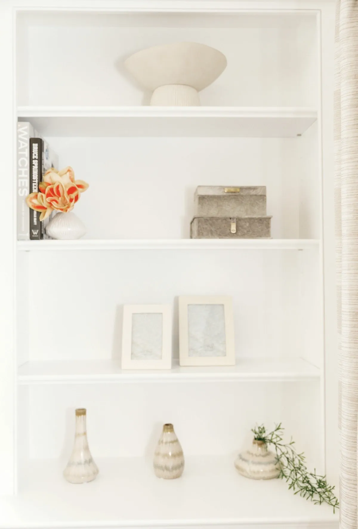 Close view of styling on white built-in shelves with orange flowers and books