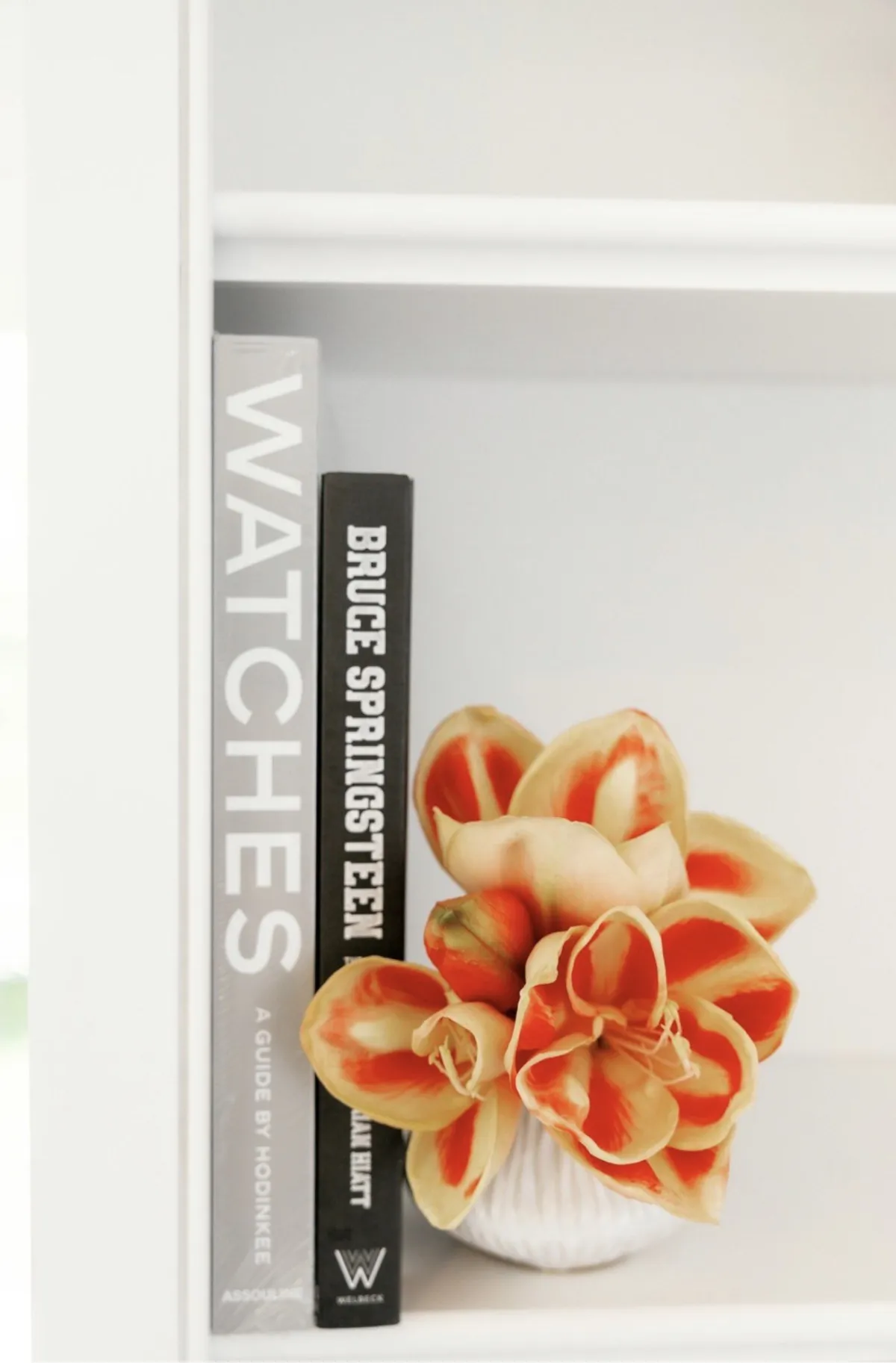 Orange flowers beside art and watch books on white shelving