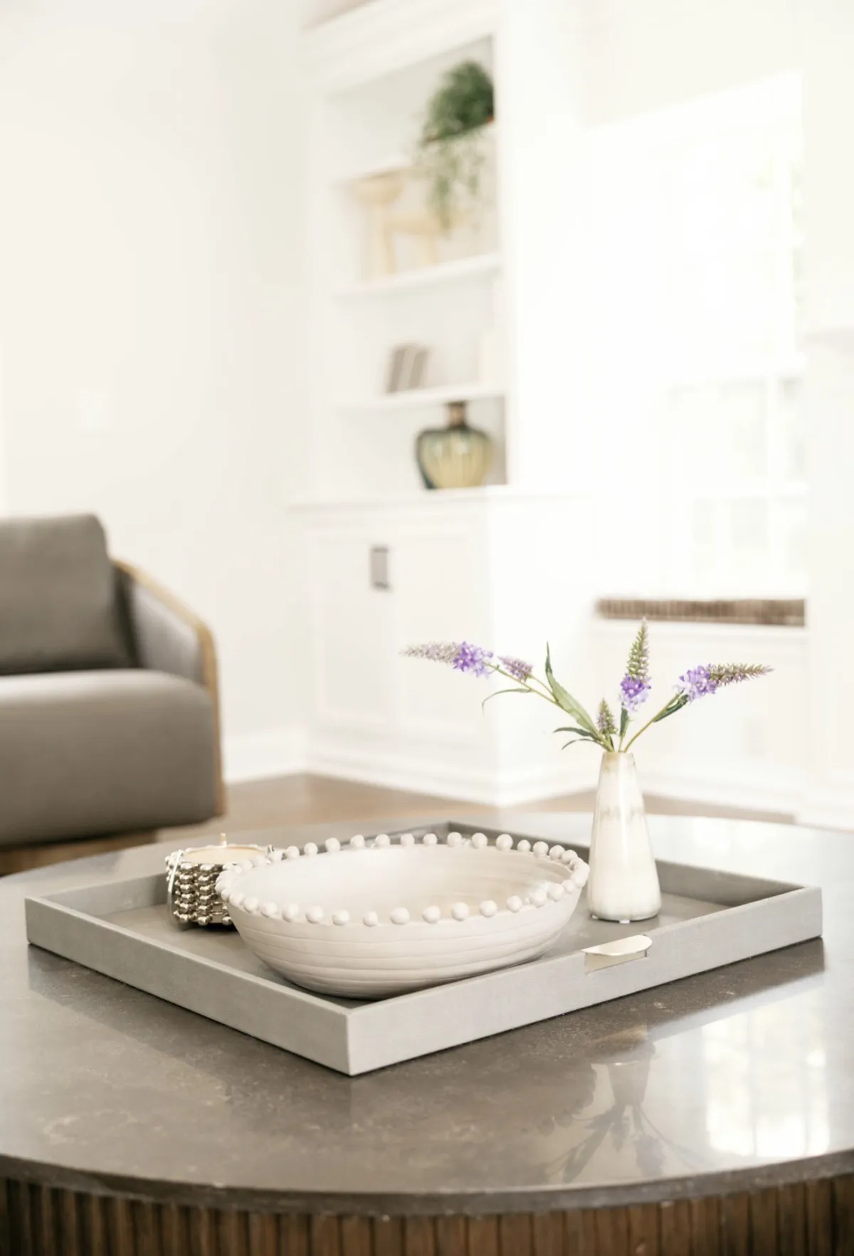 Tray, sculptural white bowl, and purple flowers on a coffee table