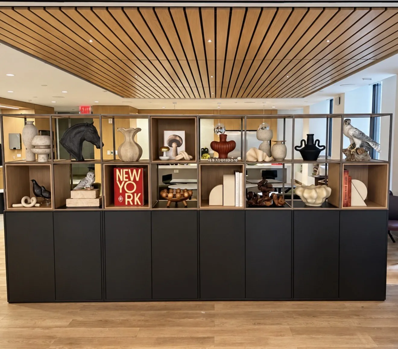 Open credenza shelving with sculpture, vessels and a New York print under a slatted ceiling