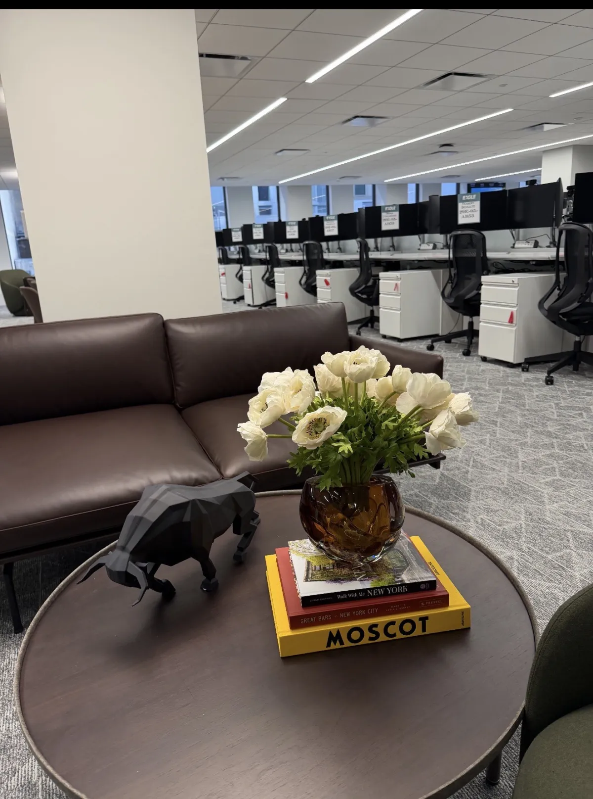 White anemones in an amber vase with a panther figurine and stacked books, open office beyond